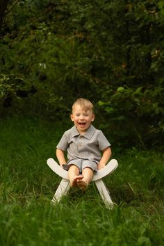 a little boy sitting on top of a chair in the grass