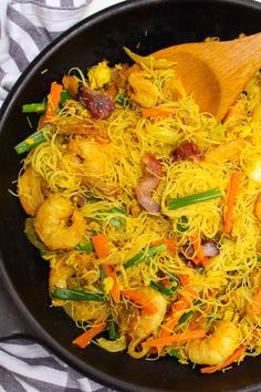 a skillet filled with shrimp, noodles and veggies next to a wooden spoon