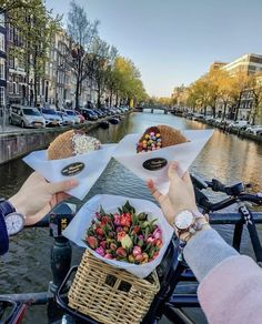 two people holding plates with flowers on them in front of the water and buildings along the canal