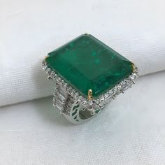 an emerald and diamond ring sitting on top of a white cloth