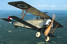 an old style airplane flying in the sky over some trees and land with two people inside it