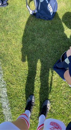 two people standing in the grass with backpacks on their backs and one person holding a cell phone