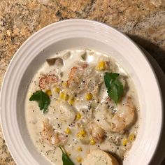 a white bowl filled with soup and shrimp on top of a marble counter next to a spoon