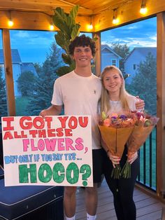 a man and woman holding flowers standing next to a sign that says i got you all these flowers but only if you're hoo?