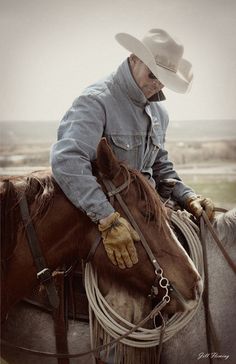 a man riding on the back of a brown horse wearing a cowboy hat and gloves