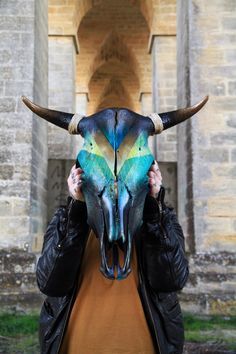 a woman holding up a bull's skull with blue and yellow paint on it