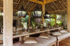 an outdoor dining area with large wooden tables and hanging lanterns over the top of it