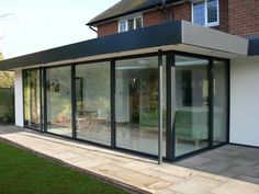 a house with glass walls and sliding doors on the outside, in front of a brick building