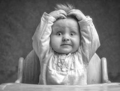 a black and white photo of a baby in a high chair with its hands on the head