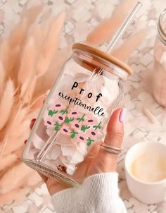 a person holding a glass jar filled with pink and green confetti next to a cup of coffee