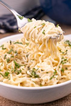 a white bowl filled with noodles and parsley on top of a wooden table next to a blue pot