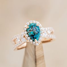 a ring with a turquoise stone surrounded by white and brown diamonds on top of a wooden stand