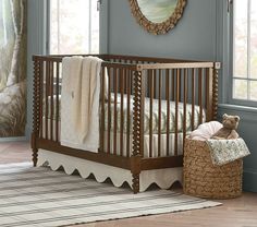 a baby crib with a teddy bear sitting in the corner next to it and a rug on the floor