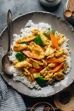 chicken and vegetable stir fry on rice in a bowl with spoons next to it