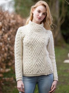 a woman standing in front of a tree wearing a white sweater and jeans with her hands on her hips