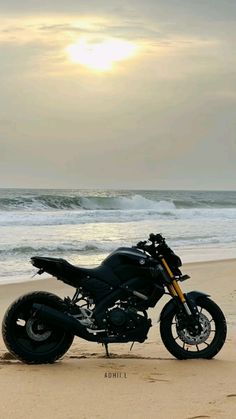 a motorcycle is parked on the beach near the water's edge as the sun sets