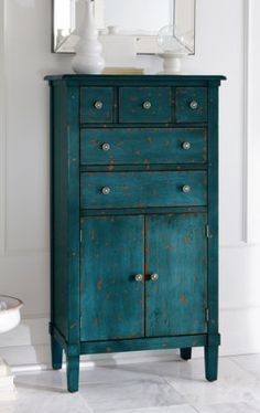 a blue chest of drawers sitting next to a mirror on top of a white wall