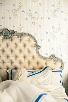 a bed with white sheets and blue trim on the headboard is in front of a floral wallpaper