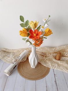 a white vase filled with colorful flowers on top of a table next to a newspaper