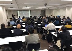 a classroom full of people sitting at desks in front of a projector screen