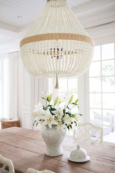 a chandelier hanging from the ceiling over a wooden table with flowers in it