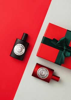 an open red gift box next to a small bottle of parfum and a green bow