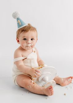 a baby sitting on the floor wearing a party hat and eating cake from a plate