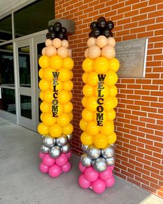 two tall yellow and silver balloons with the words welcome on them are standing in front of a brick building