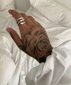 a person's hand with a rose tattoo on it, in front of a white bed