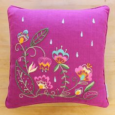 a pink pillow with flowers and rain drops on the side, sitting on a wooden surface