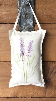 a pillow hanging on the side of a wooden wall with a metal hook and purple flowers painted on it