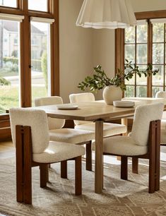 a dining room table with chairs and a vase on top of it in front of large windows