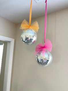 two disco balls hanging from the ceiling with pink and yellow bows on them in front of a mirror