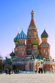 many people are walking around in front of a building that is red and white with blue domes