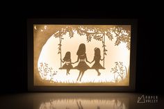 an illuminated paper cut with two girls on a swing