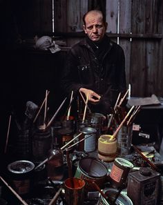 a man standing in front of a table filled with paint and brushes