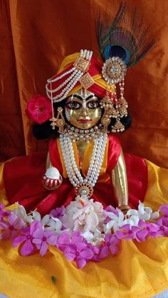 a statue of a person sitting on top of a yellow cloth covered ground with flowers