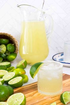 a pitcher of lemonade next to limes on a cutting board