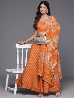 Orange and gold-toned printed lehenga choli with dupatta, gotta patti Orange and gold-toned printed ready-to-wear blouse, has a u-neck, sleeveless, zip closure Orange and gold-toned printed ready-to-wear lehenga, has a slip-on closure, flared hem Orange and gold-toned printed dupatta, border Top fabric: Poly Crepe Bottom fabric: Poly Crepe Dupatta fabric: Poly Georgette Style: Indo Western Dress, Indian Dress, Lehenga Choli, Indian Blouse With Skirt, Crop Top With Skirt and Dupatta Set Occasion: Orange Semi-stitched Palazzo Set For Navratri, Bandhani Print Sharara For Diwali Reception, Bandhani Print Sharara For Reception And Diwali, Navratri Bandhani Print Sharara For Reception, Diwali Reception Sharara With Bandhani Print, Eid Bandhani Print Sets For Reception, Orange Sets With Sheer Dupatta For Navratri, Orange Bandhani Print Sets For Eid, Orange Bandhani Print Sets For Navratri