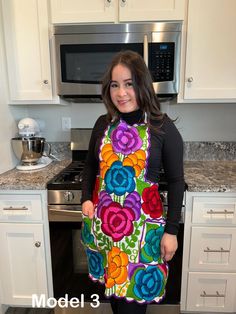 a woman is standing in the kitchen wearing an apron with colorful flowers on it and smiling