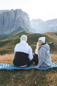 two people sitting on a blanket in the mountains