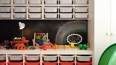 a playroom with toys and storage bins on the floor next to a chalkboard