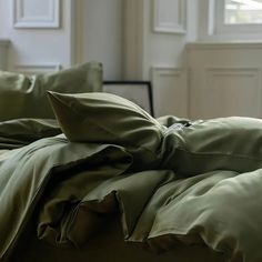 an unmade bed with green sheets and pillows