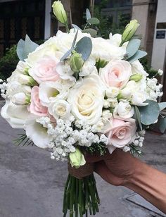 a bouquet of white and pink flowers in someone's hand on a street corner