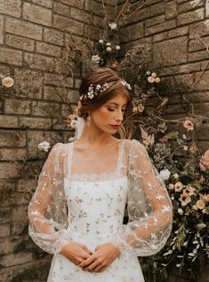 a woman standing in front of a brick wall wearing a white wedding dress with sheer sleeves