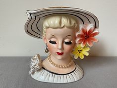 a ceramic busturine wearing a hat with flowers in it's hair and pearls around the brim