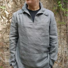 a man standing in front of a stone wall with vines growing on the side and trees behind him