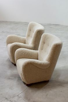 two beige chairs sitting on top of a floor next to each other in front of a white wall