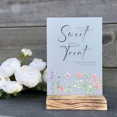 there is a card with flowers on it next to some white and pink flowers in front of a wooden stand