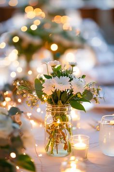 a vase filled with white flowers sitting on top of a table next to lit candles